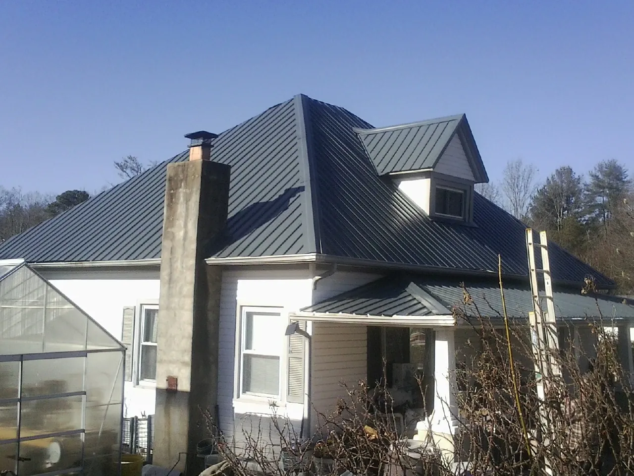 Dark blue standing seam metal roof on a white farmhouse with dormer — Slate & Tile Roof Repair by Roofing Brothers in Cullman