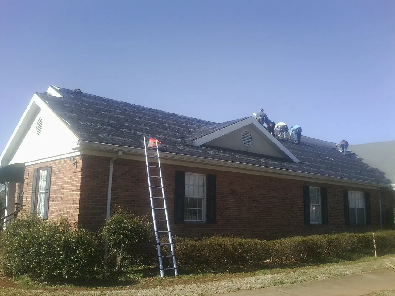 Crew tearing shingles off a brick ranch roof with a ladder set — Metal Roof Repair work by our crew in Cullman