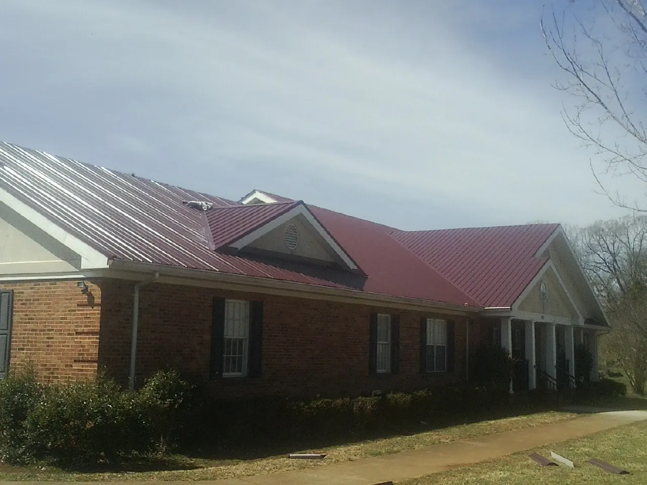 Red metal roof with gabled entries on a long brick building, from a Hail Damage Roof Repair job in Cullman