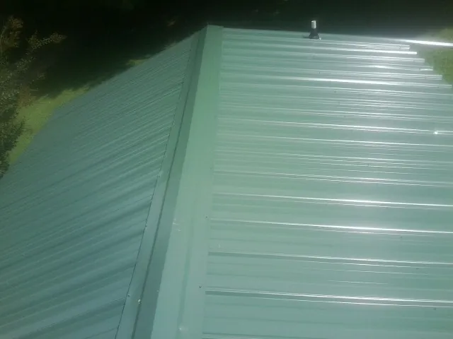 New green metal panels meeting at the ridge of a roof — Flat Roof Repair work by our crew in Cullman