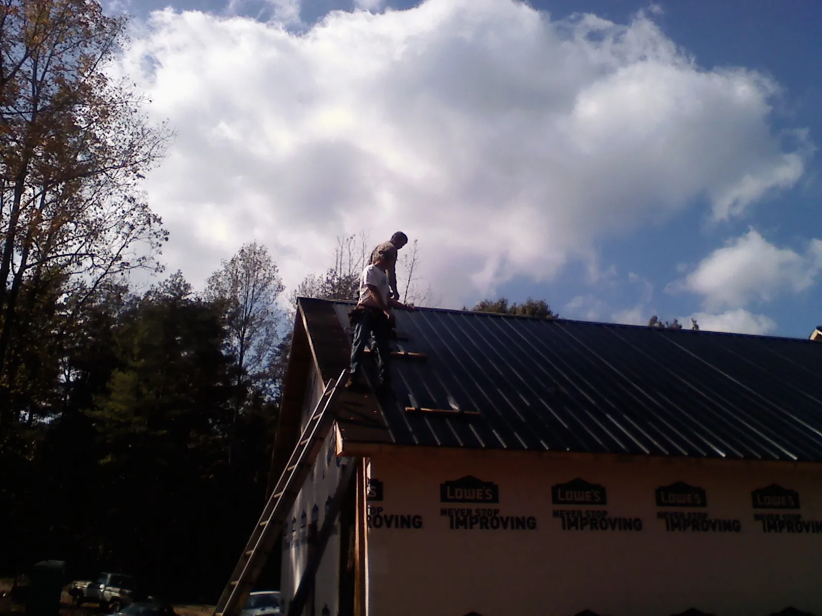 Roofer fastening dark metal panels high against a cloudy sky, from a Roof Inspection job in Cullman