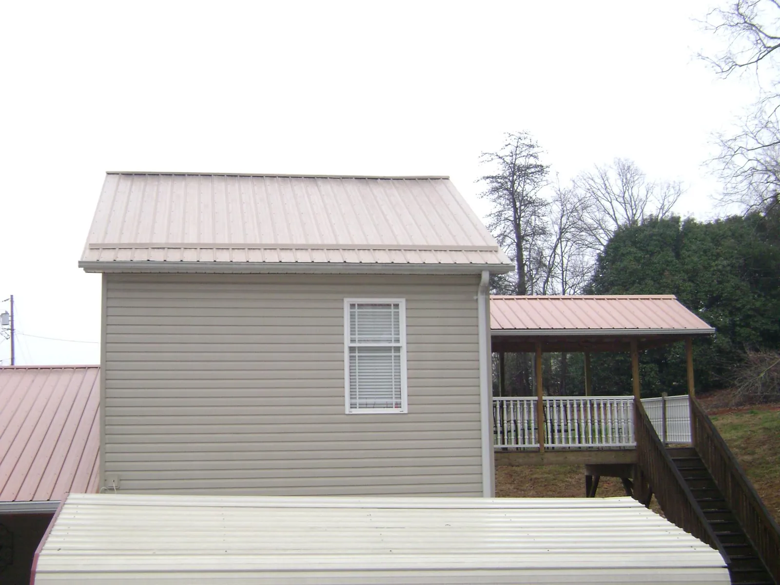 Tan metal roofs on a two story addition and attached porch, from a Roof Replacement job in Cullman